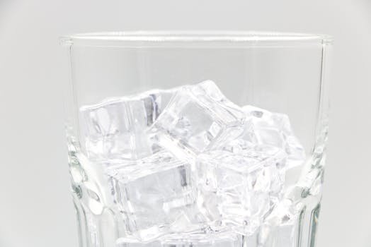 Close-up of transparent ice cubes inside a sparkling glass against a light background.